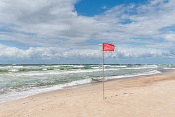 a red flag flying in a wind on a sunny windy day at a beach