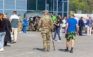 A soldier walks with a stick along a street where there are many people