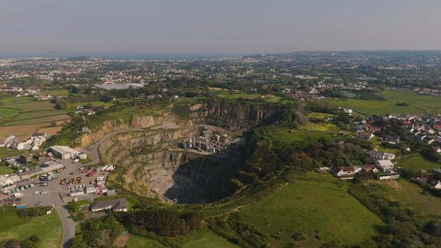 High drone shot overhead and descending into Les Vardes Quarry Guernsey showing quarry, equipment and surrounding area on bright sunny day