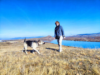 Obraz premium A middle-aged woman with a German Shepherd dog in nature in spring or autumn day with sun and blue sky. A female traveler with a pet on a trip