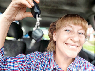 A woman is sitting comfortably in a car, holding a car key in her hand