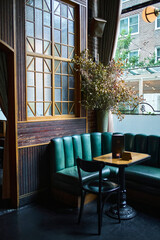 Emerald green corner bench nook. Cafe table and seating below large windows. 