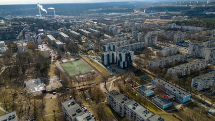 Fototapeta premium Aerial view of a modern urban area featuring a mix of residential and commercial buildings, with green spaces and parking lots. The skyline includes various structures.