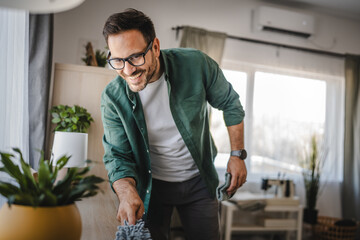 Fototapeta premium Adult man clean a desk with a microfiber cloth in a cozy living room