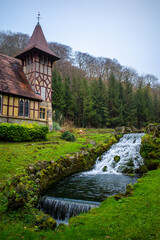 A small stream flows through a lush green field, with a church in the background