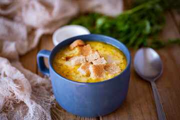 A hearty lunch for the family: onion soup with cheese and crackers in a beautiful plate on a wooden table. Cheese soup with vegetables in a blue plate with croutons. Close-up