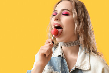 Young woman eating lollipop on yellow background, closeup