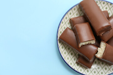 Plate with tasty chocolate covered coconut candies on blue background