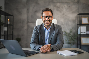 Portrait of confident businessman sit at the desk and smile in office