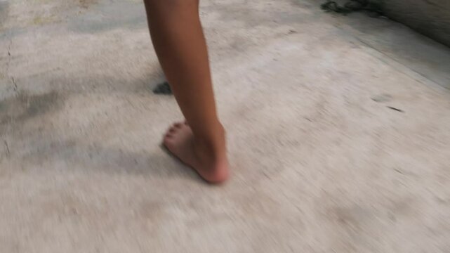 A young child walks barefoot on the concrete surface on a bright sunny day.