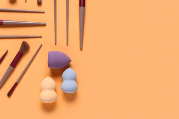 Makeup sponges and brushes on orange background