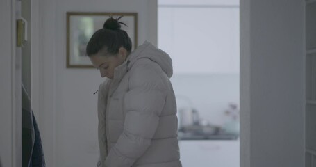 Woman putting on a jacket in the hallway, preparing to leave the house, followed by picking up her purse, getting ready for the day in a casual home environment