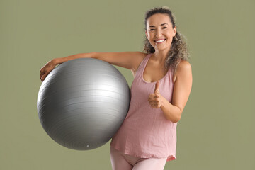 Beautiful adult woman in sportswear with fitness ball on green background