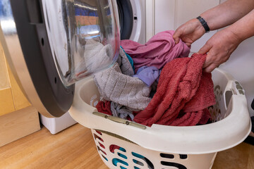 Woman unloading laundry from a front-loading washing machine into a laundry basket, featuring towels and clothing