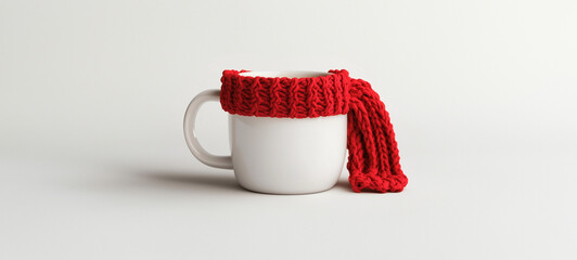 A white coffee mug with a red knitted scarf wrapped around it, isolated on a solid background