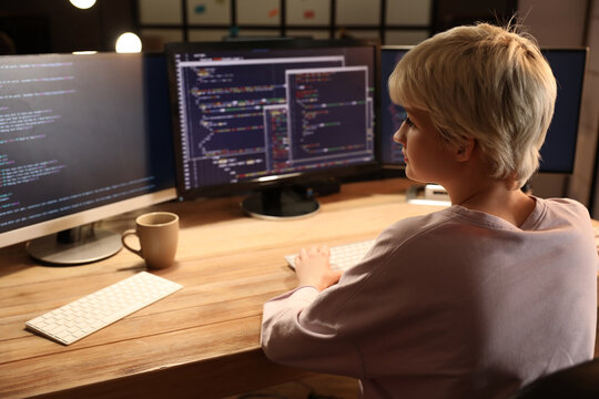 Female programmer working with computer in office at night, back view