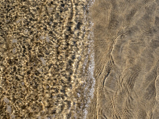 Rippled, shallow water surface with visible beach sand texture.