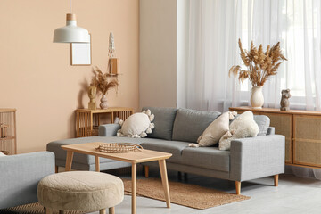 Interior of stylish living room with grey sofa, wooden table and pampas grass