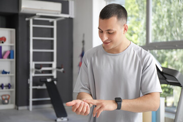 Sporty young man checking pulse in gym