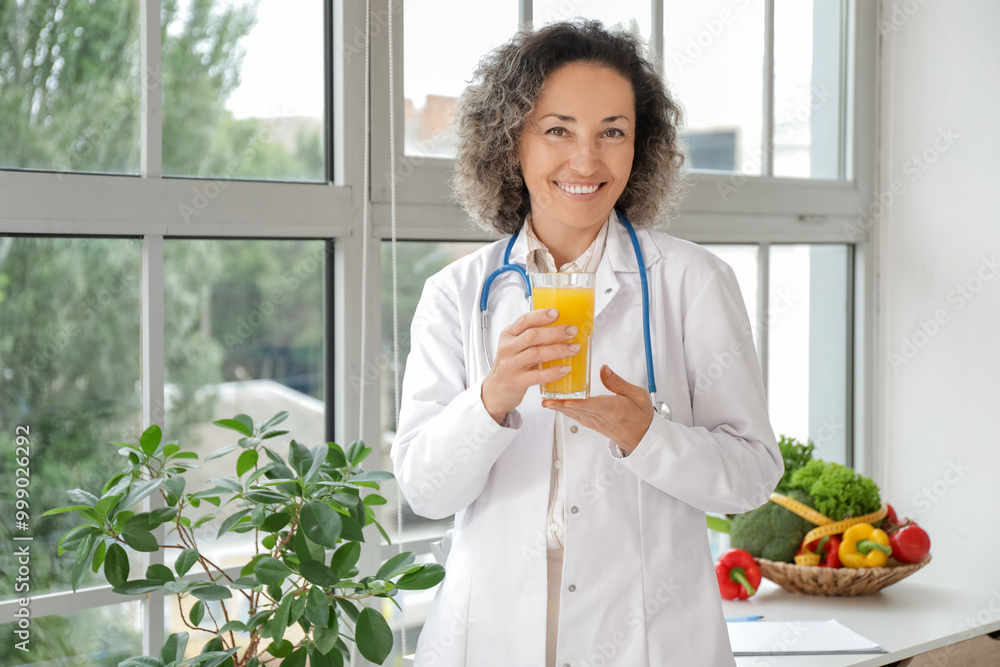 Poster Mature female nutritionist with glass of juice in office