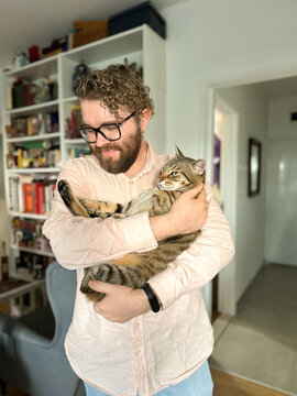 Handsome millennial man holds a tabby cat in his arms and kisses it. Pet and friendship concept