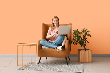 Young beautiful woman sitting on armchair and using laptop at home
