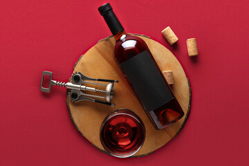 Wooden tray with bottle, glass of wine, corks and opener on red background