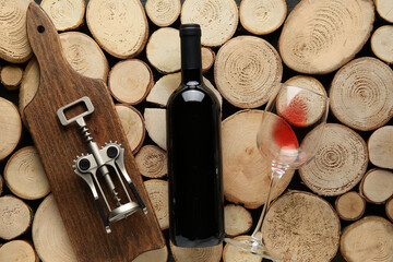 Bottle of red wine, glass, board and opener on wooden background