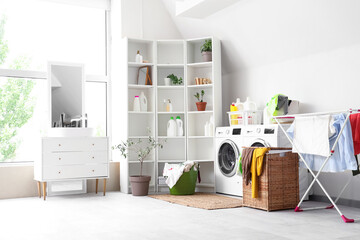 Interior of light bathroom with washing machines, laundry basket and dryer