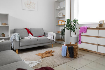 Interior of living room with laundry basket and dirty clothes on sofa