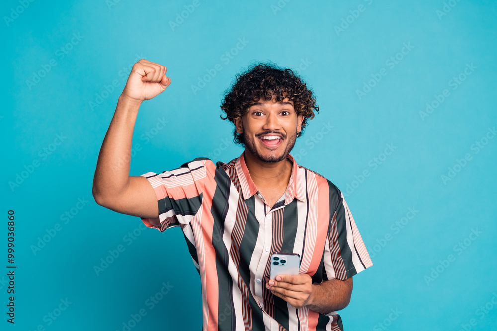 Wall mural Photo of attractive funny guy wear striped shirt winning game modern gadget emtpy space isolated blue color background