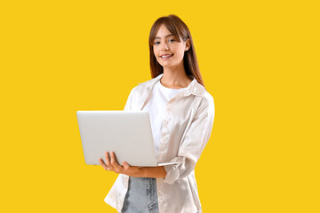 Beautiful young woman using laptop on yellow background