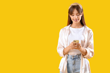 Beautiful young woman using mobile phone on yellow background