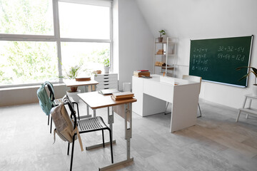 Interior of empty classroom with desks, teacher's table and blackboard