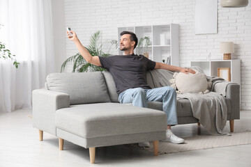 Fototapeta premium Handsome young man switching on air conditioner at home