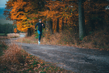 Fototapeta premium A young man, clad in athletic wear, strides confidently along a path through a vibrant autumn forest