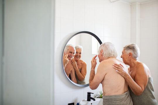Elderly couple examining their skin in bathroom mirror