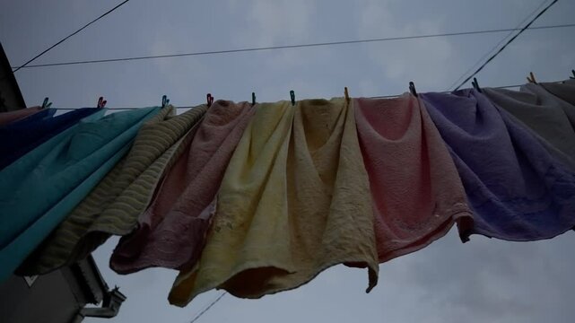 Colorful clothes are drying on a clothesline. The wind is gently blowing the clothes, creating a relaxing and peaceful scene. Shot in slow motion