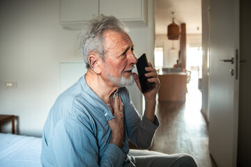 Senior man feeling chest pain while talking on smartphone at home