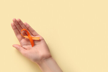 Fototapeta premium Female hand with orange ribbon on yellow background. World Cancer Day