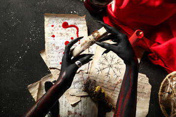 Bloody witch hands with magic attributes and spell paper sheets on grunge black background, top...