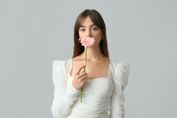 Beautiful young woman with pink gerbera flower on grey background