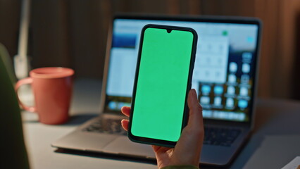 Girl hand holding chromakey cellphone working late at home office close up. 