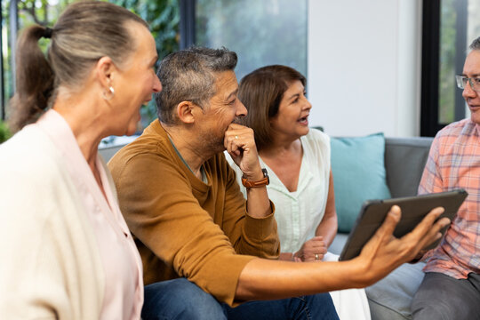 Laughing together, senior diverse friends using tablet and enjoying conversation on couch, at home