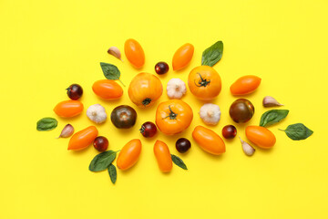 Different fresh tomatoes with garlic and basil on yellow background