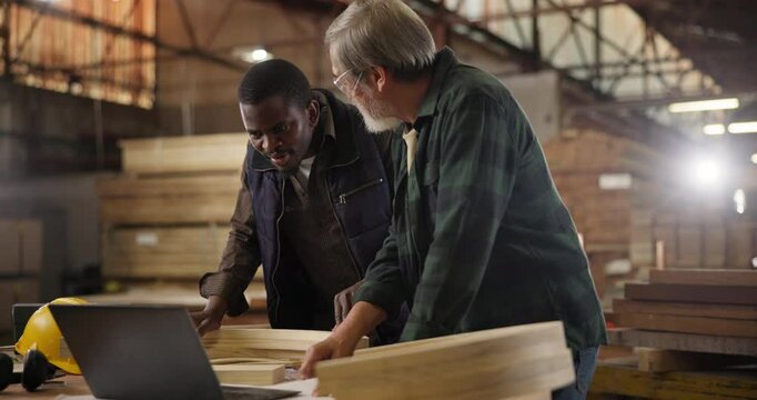 Teamwork, carpenter and laptop in workshop, apprentice and designer furniture manufacturing. Mentorship, carpentry and men at sustainable business, teaching and learning with computer for job project