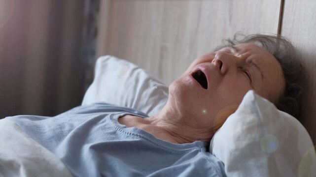 An elderly woman sleeps with her mouth open and snores, close-up