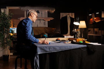 Senior expert suitmaker alone in upscale tailoring studio, designing upcoming fashion collection....