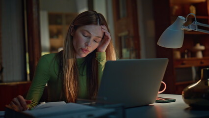 Night worker closing computer feeling overworked in dark apartment close up.