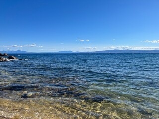 Sunlit Coastal Boat on Clear Blue Waters – Peaceful scenic view of a boat floating near a rocky shoreline under a bright sun and clear sky in the Mediterranean